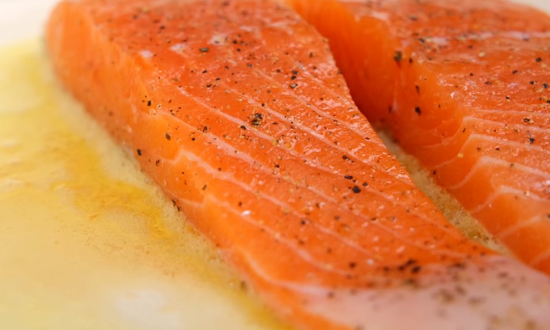 Two pieces of salmon cooking on oil in a pan