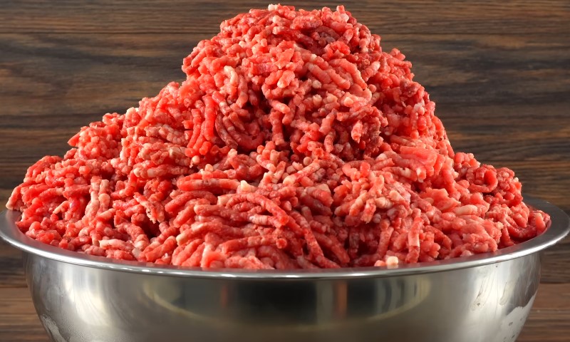 A person holding a tray of ground beef in front of a shelf filled with various food items