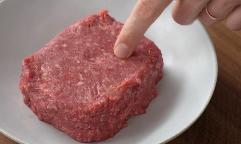 A person touches a piece of meat on a plate