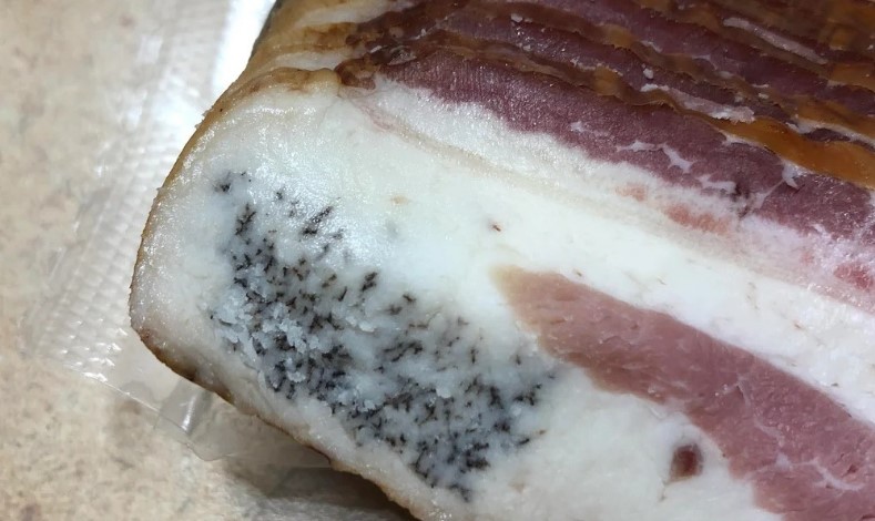 Detail shot of bacon or pork belly exhibiting unusual black crystalline or mold-like specks
