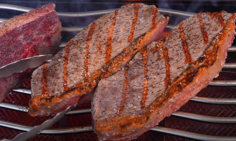 Two steaks, seasoned with salt and pepper, displaying distinct grill marks while cooking over heat