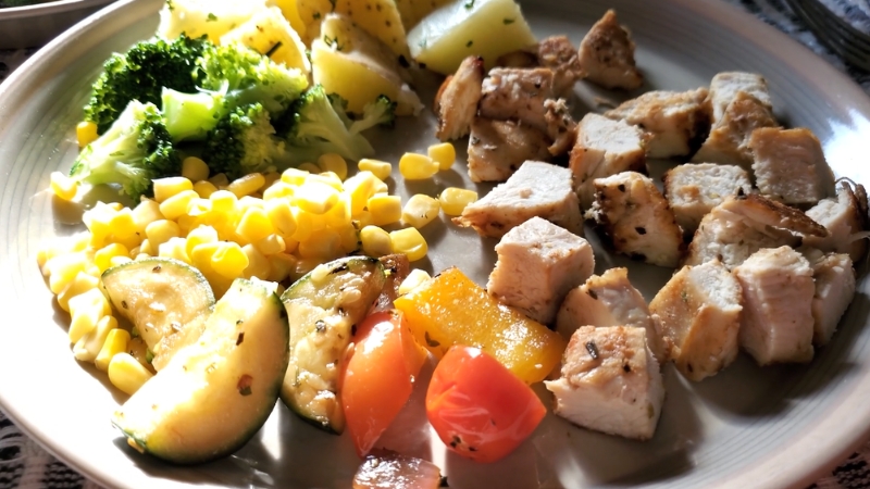 Grilled chicken with potatoes, corn, broccoli, and zucchini on a plate as a balanced carb-focused training meal